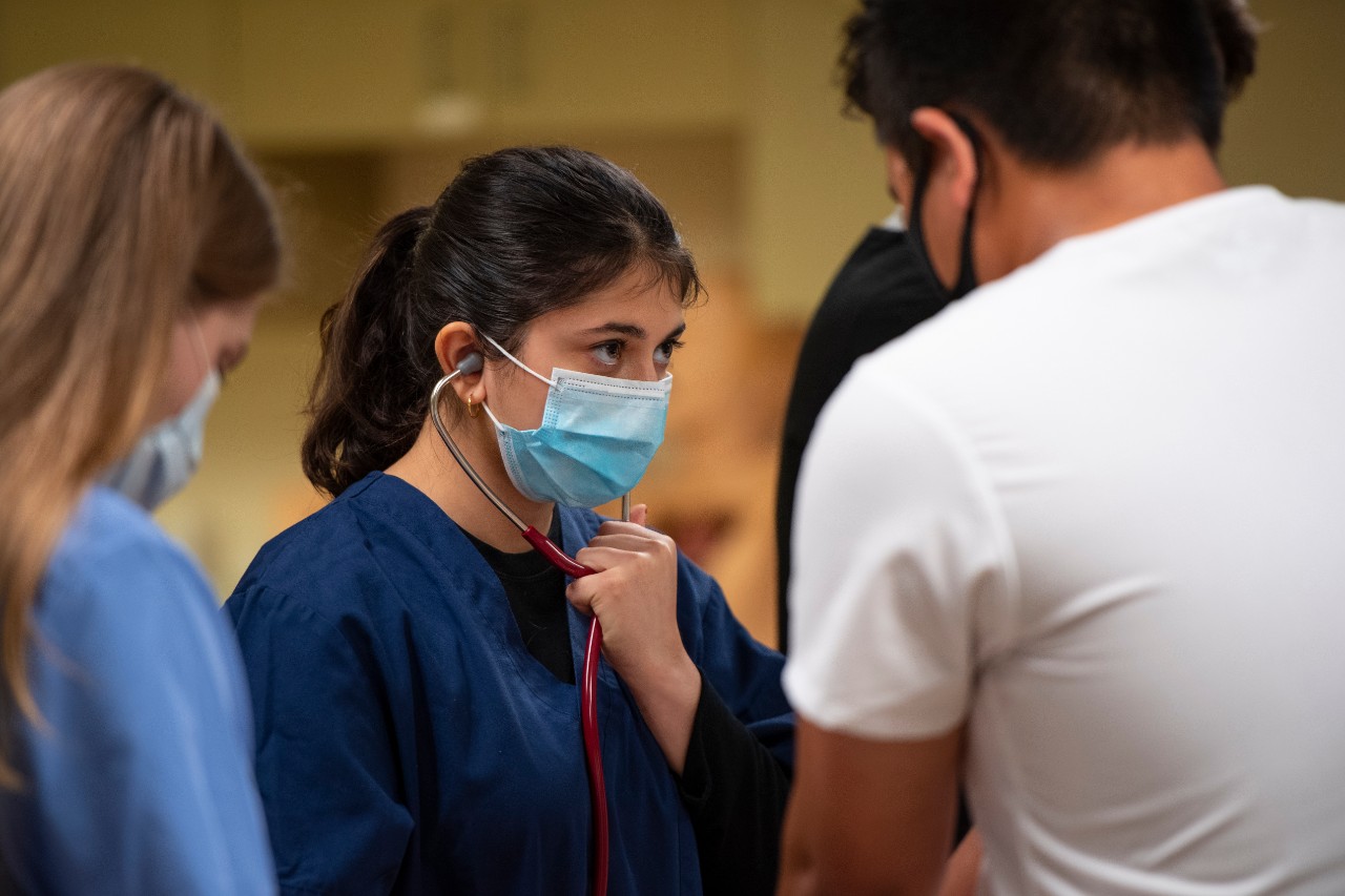 nurse wearing scrubs and listening through a stethoscope near other nurses